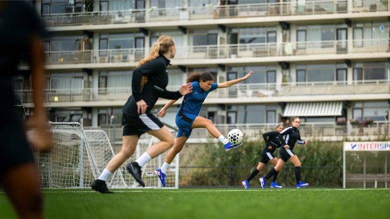 4 Mädchen die in blauen Trikots Fußballspielen im Hintergrund ist ein INTERSPORT Logo zu sehen