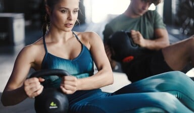 Eine Frau und ein Mann trainieren mit Kettlebells im Fitnessstudio.