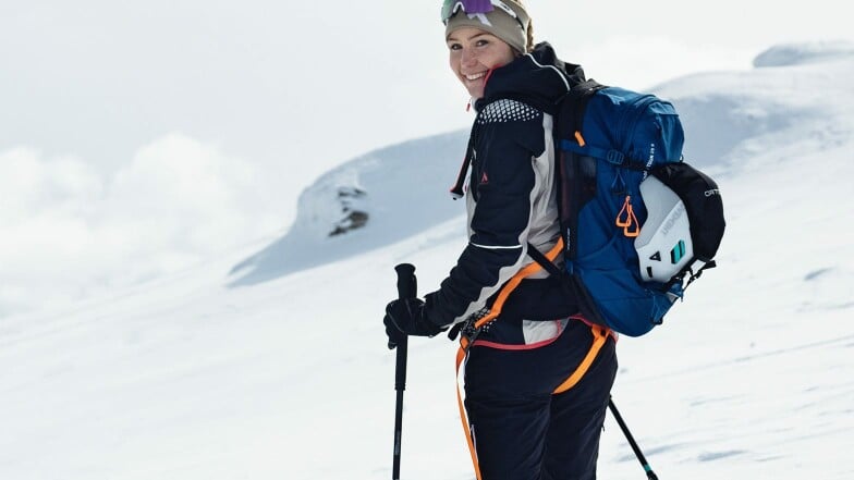 Eine glückliche Frau auf Skitour in einer verschneiten Berglandschaft.