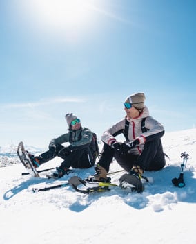 Zwei Personen machen eine Pause bei einer sonnigen Schneeschuhwanderung.
