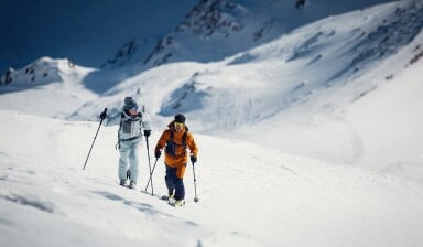 Zwei Personen auf einer Skitour in den verschneiten, sonnigen Bergen.