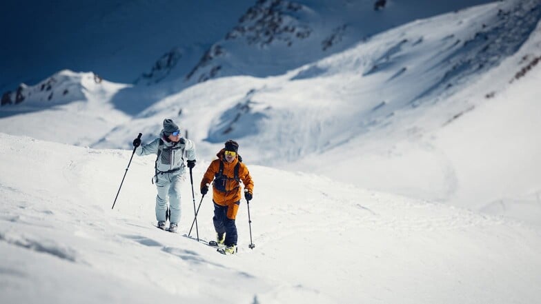 Zwei Personen auf einer Skitour in den verschneiten, sonnigen Bergen.