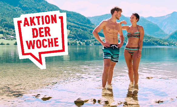 Paar in Badebekleidung steht in einem See vor Berglandschaft, daneben der Schriftzug »AKTION DER WOCHE«
