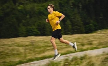 Mann in gelbem Shirt joggt auf einem Weg durch eine Landschaft mit Bäumen im Hintergrund.