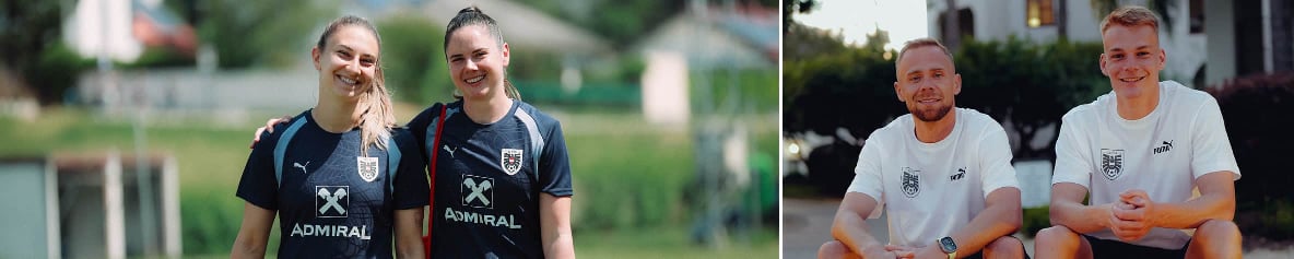 Zwei Sportlerinnen in Trainingskleidung gehen auf einem Rasenplatz, daneben sitzen zwei Sportler in weißen Shirts.
