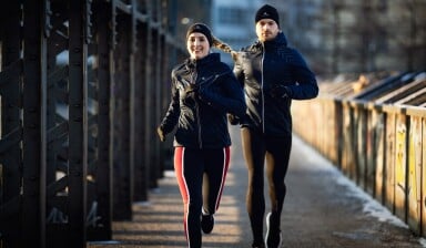 Ein Mann und eine Frau joggen im Winter auf einer Brücke.