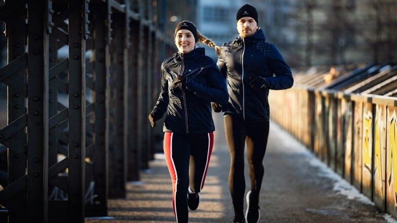 Ein Mann und eine Frau joggen im Winter auf einer Brücke.