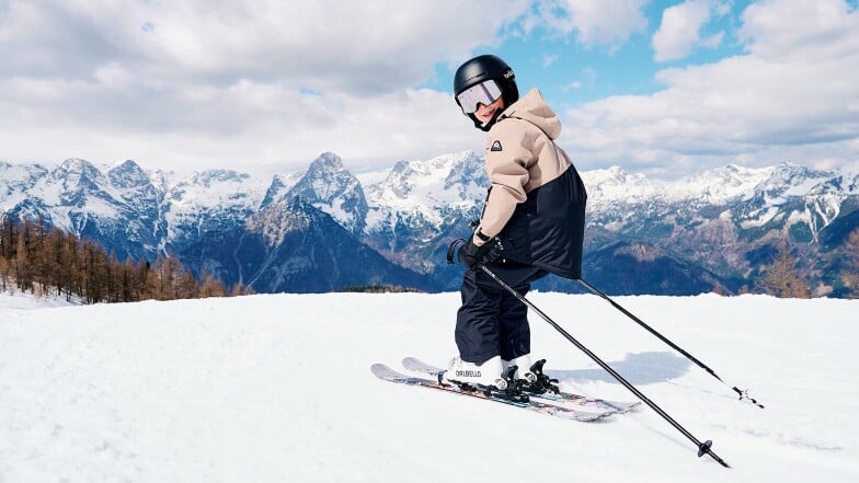 Ein lächelndes Kind fährt Ski auf einer Piste in den Bergen.