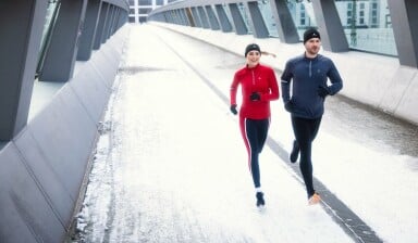 Mann und Frau joggen zusammen im Winter auf einer Brücke.