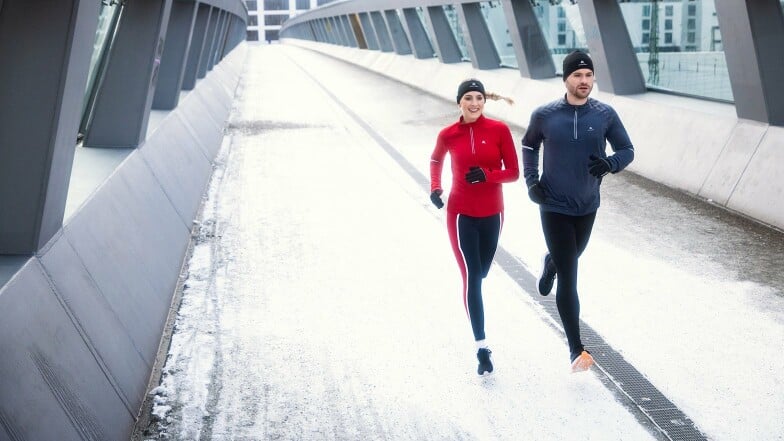 Mann und Frau joggen zusammen im Winter auf einer Brücke.