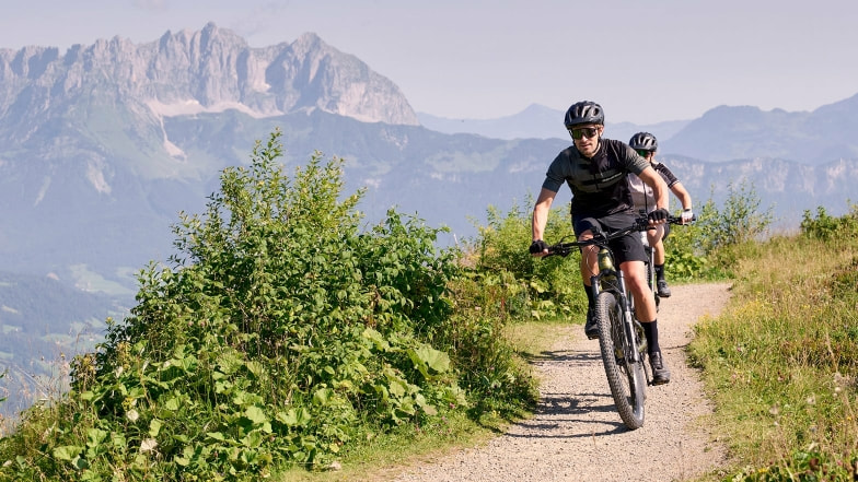 Zwei Mountainbiker fahren auf einem Schotterweg in den Bergen.