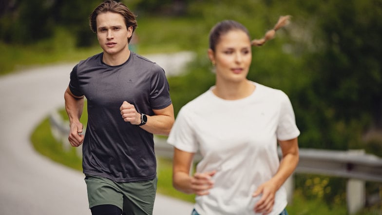 Eine Läuferin und ein Läufer bei einem gemütlichen Lauf im Sonnenschein.