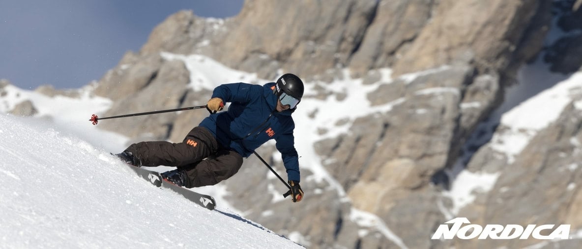 Ein Skifahrer fährt eine Kurve auf einer schneebedeckten, sonnigen Piste.