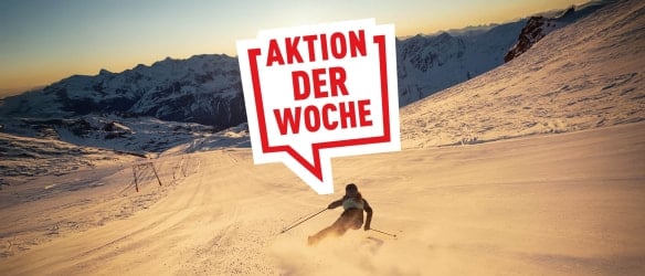 Eine Person fährt bei Sonnenuntergang auf einer Skipiste, im Vordergrund steht ein rotes Werbeschild mit der Aufschrift „Aktion der Woche“.