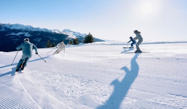 Vier Skifahrer auf einer sonnigen Piste in den verschneiten Bergen.