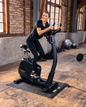 Eine Frau trainiert auf einem Fahrradergometer in einem Fitnessraum.