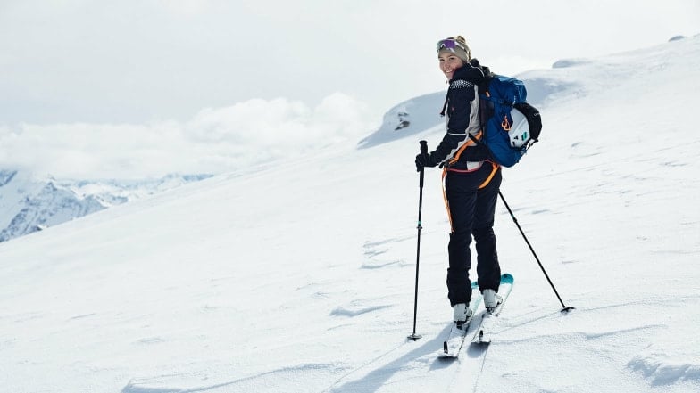 Eine lächelnde Frau auf Skitour in den verschneiten Bergen.