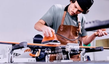 Ein Mann wachst konzentriert ein Paar Skier in einer Werkstatt.