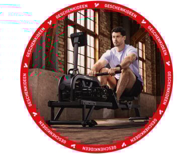 Mann trainiert auf einem Rudergerät in einem Raum mit Backsteinwänden.