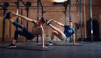 Mann und Frau machen synchron eine Dehnübung im Fitnessstudio.