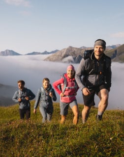 Dva muži a dvě ženy jdou v outdoorovém oblečení po horách s mraky v pozadí.