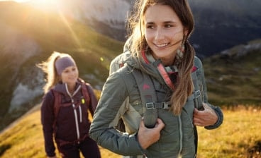 Dvě ženy na horách při západu slunce v outdoorovém oblečením a s batohy.