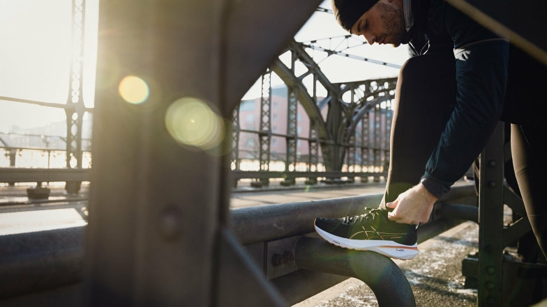 Ein Läufer bindet seinen Schuh auf einer Brücke im Sonnenlicht.