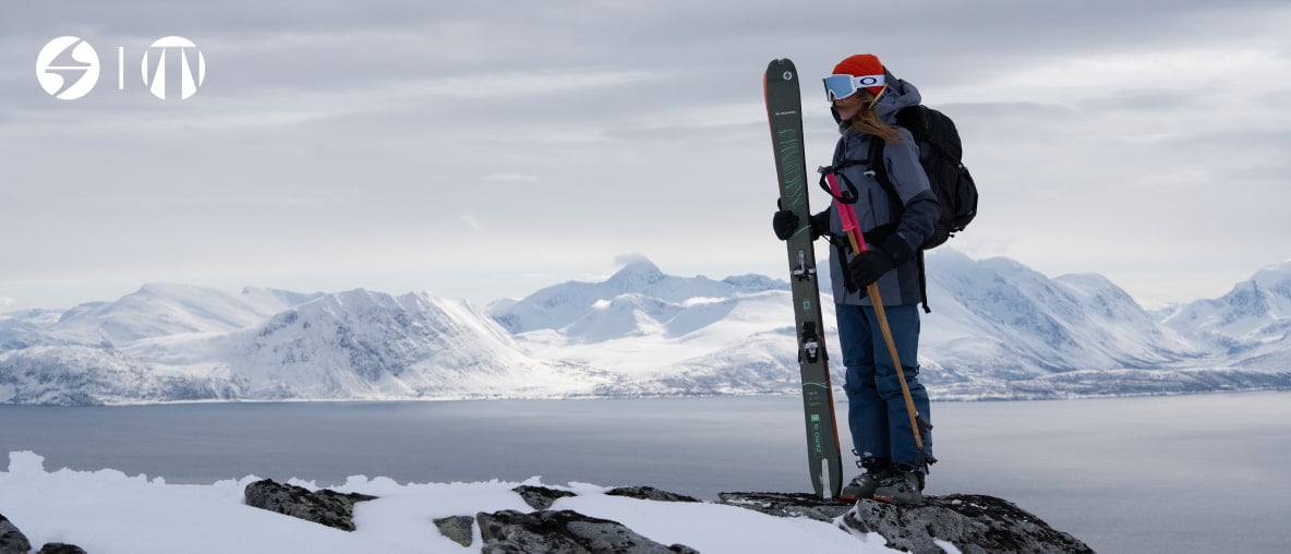 Eine Skifahrerin steht auf einem Berg mit Blick auf Fjord.