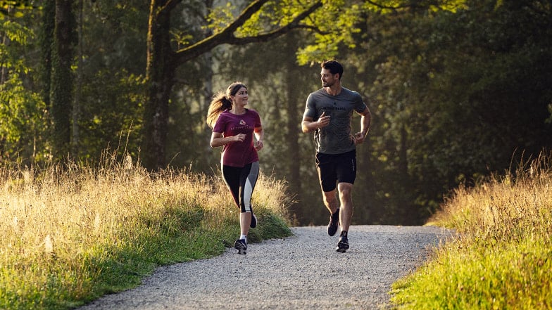Ein Paar joggt gemeinsam auf einem Schotterweg in der Natur.