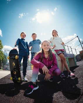 Vier Kinder mit Skateboard auf einem Skateplatz unter blauem Himmel