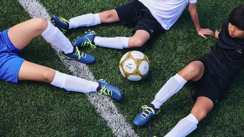 Drei Jungs machen erschöpft Pause sitzend am Fußballfeld.