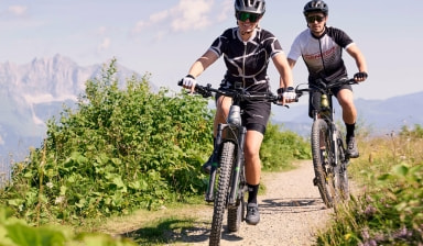 Zwei Personen fahren Mountainbike auf einem Weg in den Bergen.