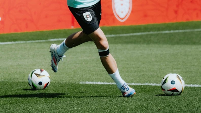 Die Beine eines Fußballspielers beim Dribbling im Training, zwei Fußbälle liegen auf dem Rasen.