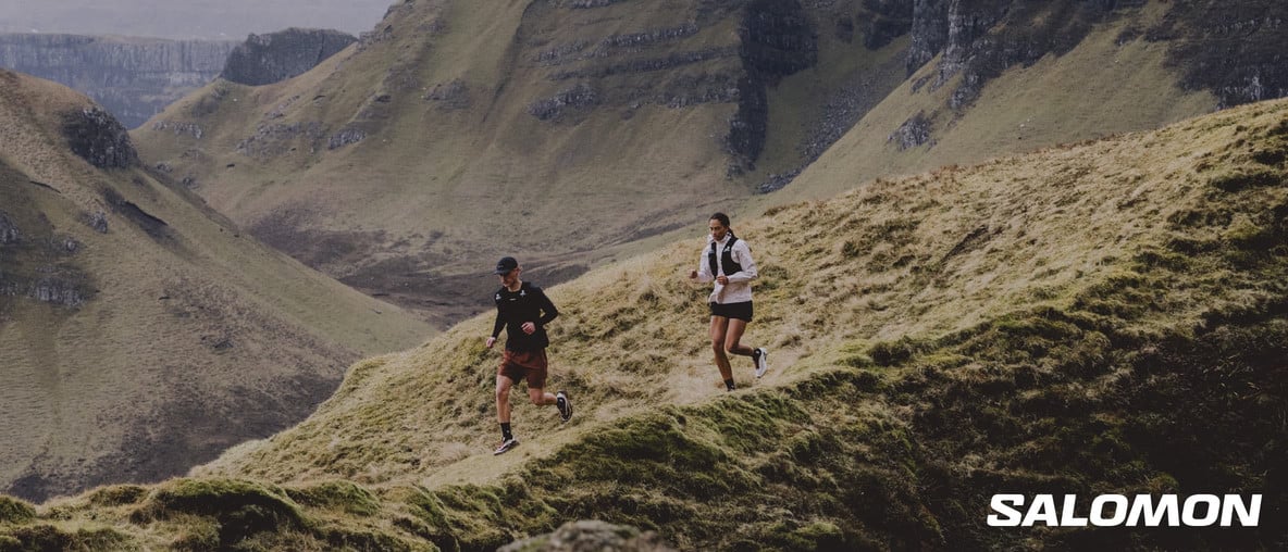 Eine beeindruckende Berglandschaft und mittendrin eine Frau und ein Mann laufend mit Ausrüstung von Salomon.