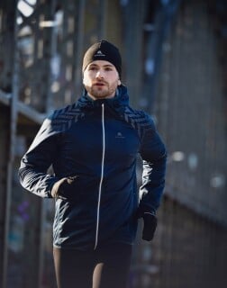 Ein Läufer in dunkler Laufkleidung läuft konzentriert über eine Brücke.