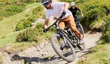 Zwei Personen fahren mit Mountainbikes auf einem Bergpfad bergab.