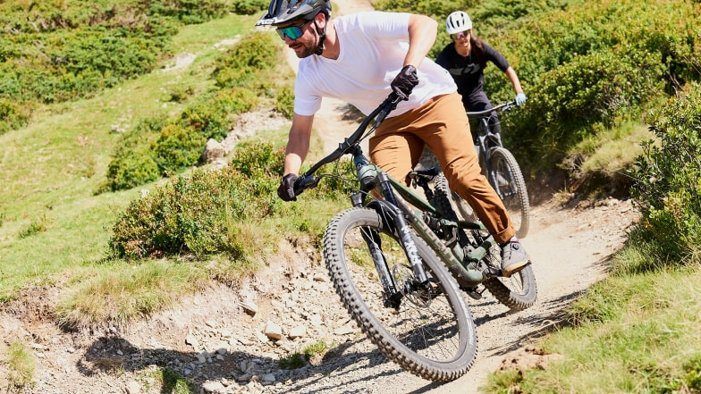 Zwei Personen fahren mit Mountainbikes auf einem Bergpfad bergab.