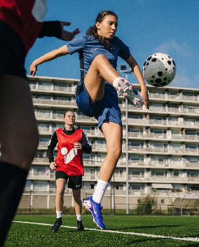 Fußballspielerin in blauem Trikot tritt auf einem Fußballplatz nach dem Ball