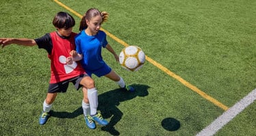 Ein Mädchen und ein Junge bei einem Fußballspiel im Zweikampf um den Ball.