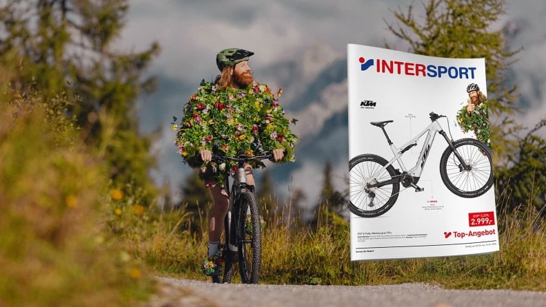 Der Frühling mit einem Fahrrad in einer Berglandschaft. Im Vordergrund die Titelseite des INTERSPORT Flugblatts.