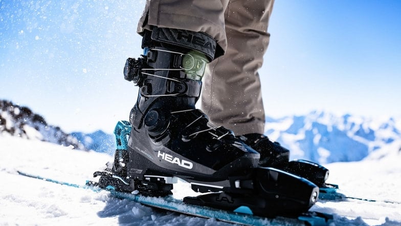 Nahaufnahme von schwarzen Head-Skischuhen auf Skiern im verschneiten Gebirge.