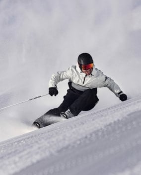 Ein Mann mit Skihelm von bollé fährt Ski auf einer präparierten, verschneiten Piste.