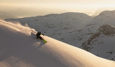 Ein Skifahrer fährt durch Pulverschnee in den Bergen bei Sonnenuntergang.