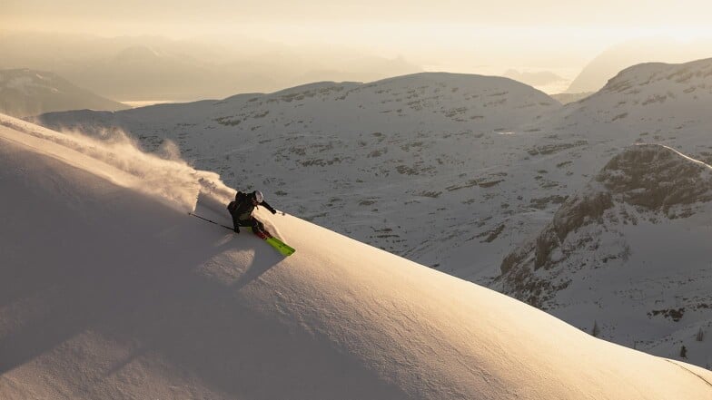 Ein Skifahrer fährt durch Pulverschnee in den Bergen bei Sonnenuntergang.
