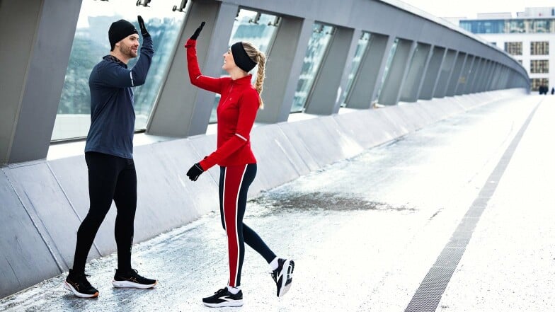 Zwei Läufer geben sich nach dem Sport auf einer Brücke High-Five.