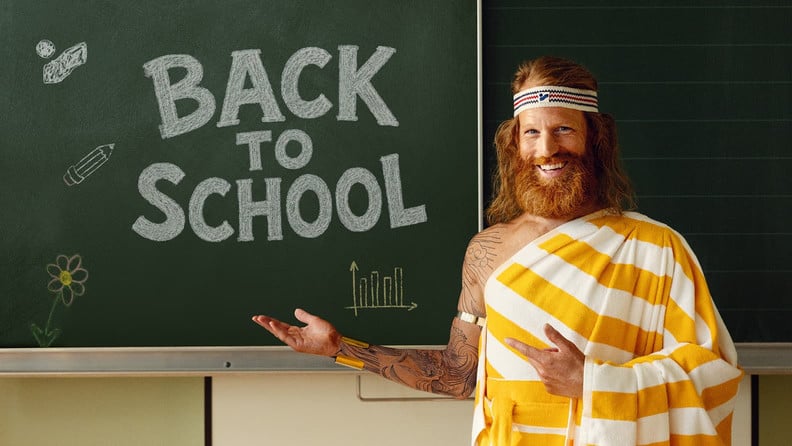 Der Sommer steht vor einer dunkelgrünen Schultafel, auf der mit weißer Kreide "Back To School" geschrieben steht, und lächelt fröhlich.