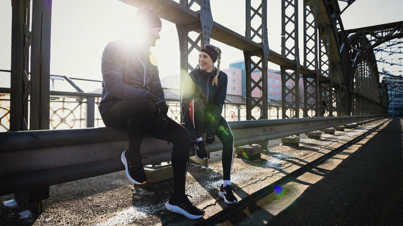 Zwei Läufer machen eine Pause auf einer sonnigen Brücke.