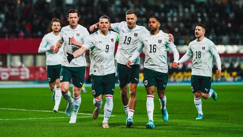 Mehrere Fußballspieler in weißen Trikots laufen gemeinsam jubelnd über das Spielfeld.