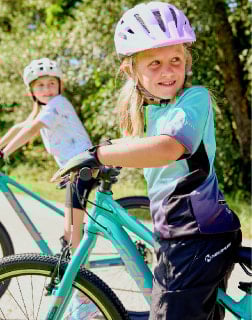 Dvě dívky sedí na kolech v cyklistické výbavě s helmami.