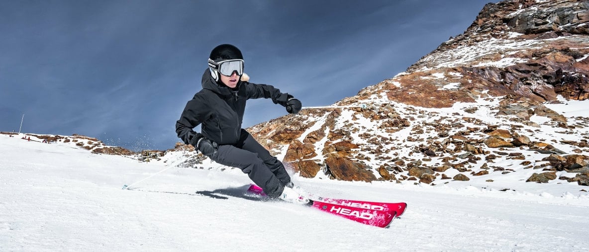 Eine Skifahrerin fährt eine Kurve auf einer schneebedeckten Piste mit einem Ski von Head.